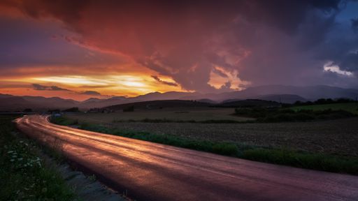 A beautiful shot of a narrow curvy road in the countryside in the middle of a field at sunset