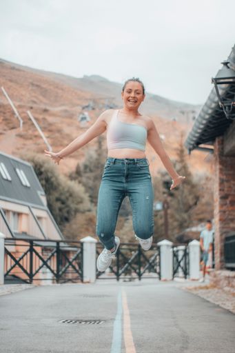 A vertical shot of a young girl jumping on the road of a village in the mountains
