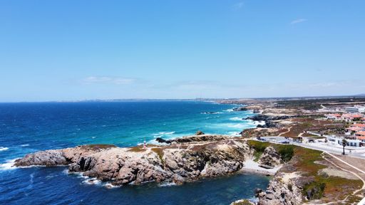 A drone view of a rocky beach with ocean waves crashing on the shore with houses