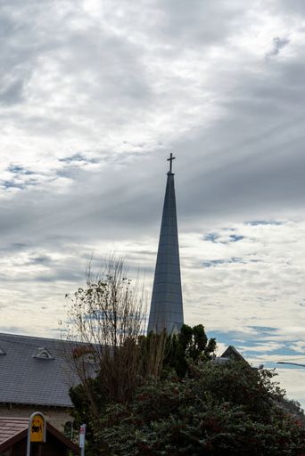 A low angle shot of a church dome with a cross on top against a cloudy blue sky