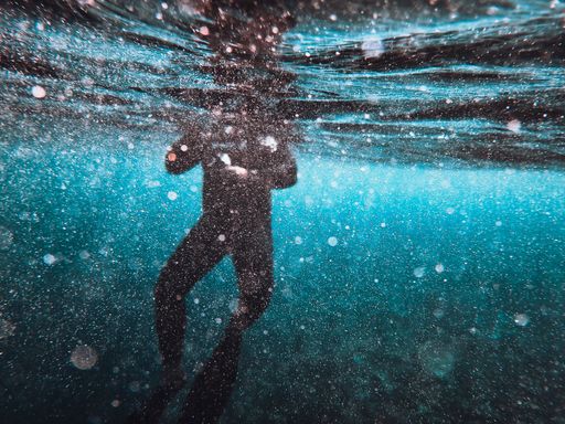 A diver swimming on a sea surface with sunlight passing through the water