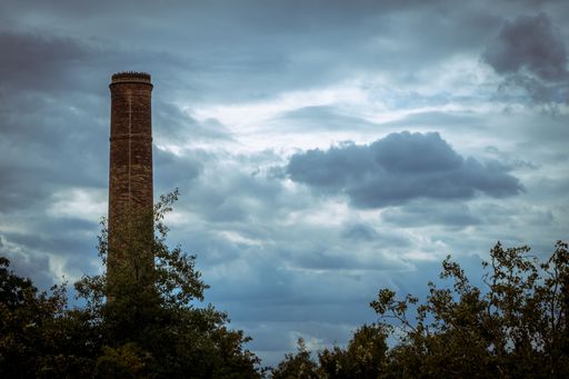 An old brick factory chimney in a forest with an overcast in the background