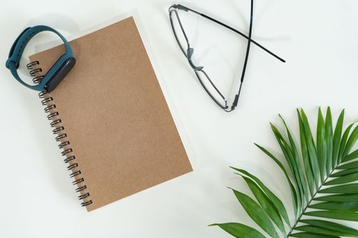 A top view of notebooks, eyeglasses, watches, and plants on a white table