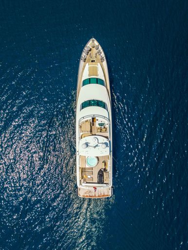 A vertical aerial top view of a luxurious yacht in the beautiful blue sea