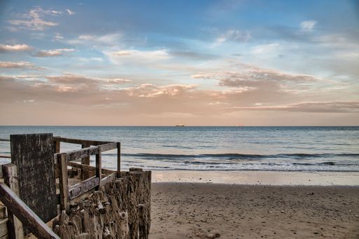 A view of the wooden structure on the sandy shore before the seascape at sunset