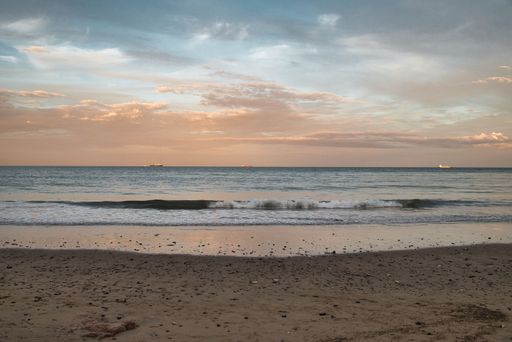 A view of the sandy shore before the seascape under the cloudy sunset sky