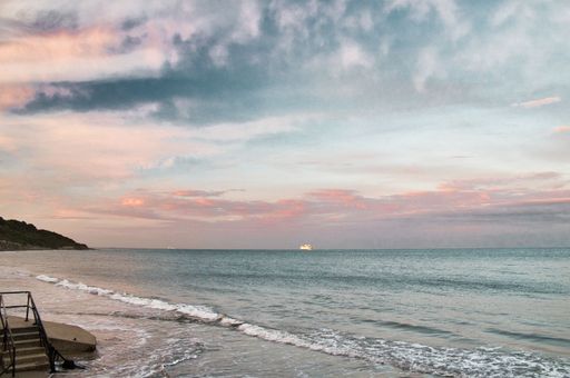A view of the sandy shore before the seascape under the cloudy sunset sky