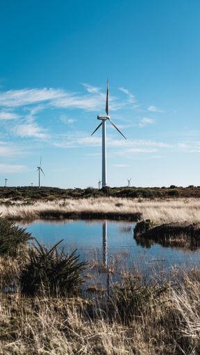 A windmill in a dry grass field by a lake
