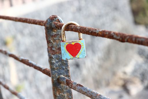 A closeup shot of a rusty padlock with a painted red heart locked on a rusty bridge