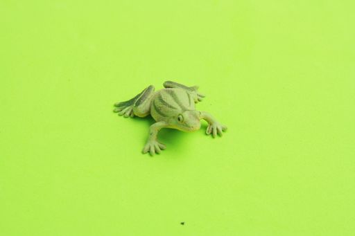 A closeup shot of a plastic frog toy miniature on a green surface