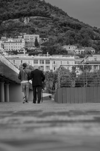 A grayscale shot of an old man and a young woman walking