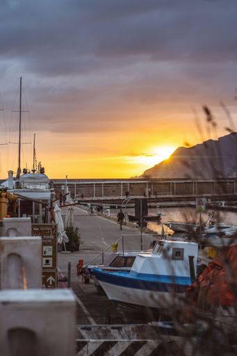 A vertical shot of a small harbor with boats against the golden sunset behind a mountain