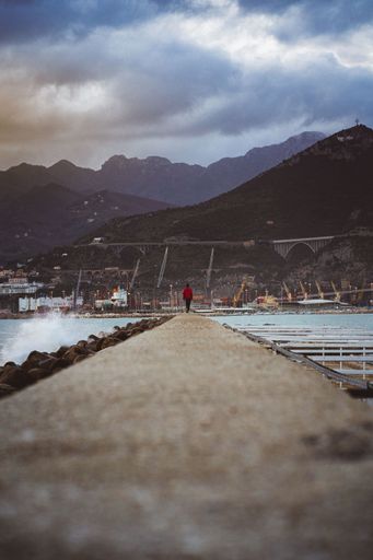 A vertical shot of a man on the dock walking to the mountains - cloudy weather