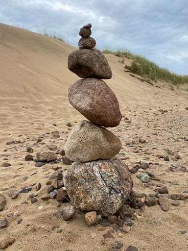 A vertical shot of a stack of stones over the sand under a blue cloudy sky