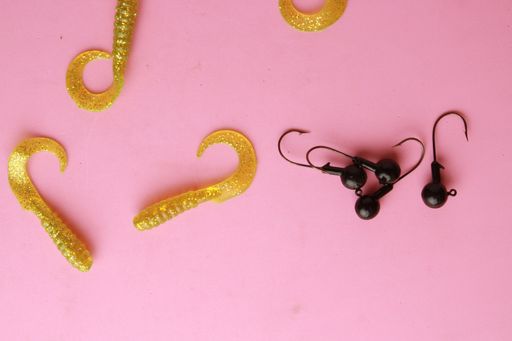 A top view of colorful different fishing lures and hooks on a pink background
