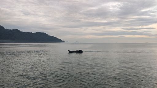 A  silhouette of a fishing boat in a sea bay the background of rocks during sunset