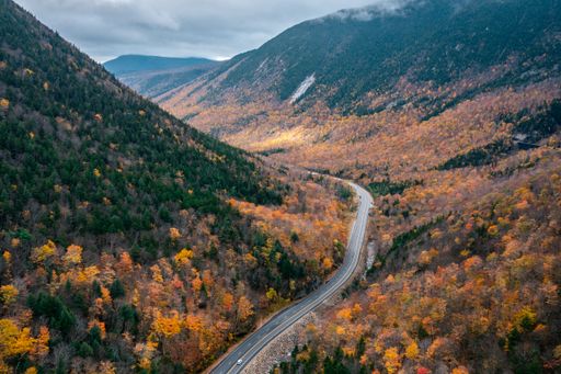 An aerial view of a road through orange autumn trees in White Mountain National Forest, New Hampshire