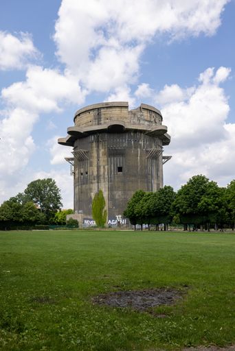 A vertical shot of a Flak tower surrounded by trees under the cloudy blue sky in Vienna, Austria