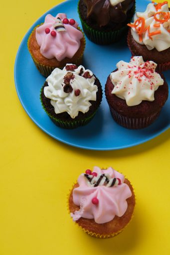 A vertical closeup shot of small cupcakes with colorful creams on a blue plate with yellow background
