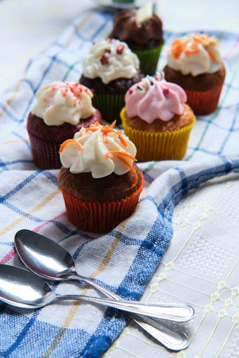 A closeup shot of small cupcakes with colorful creams and two teaspoons on a kitchen towel