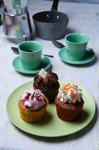 A closeup shot of small cupcakes with colorful creams and coffee cups in the background
