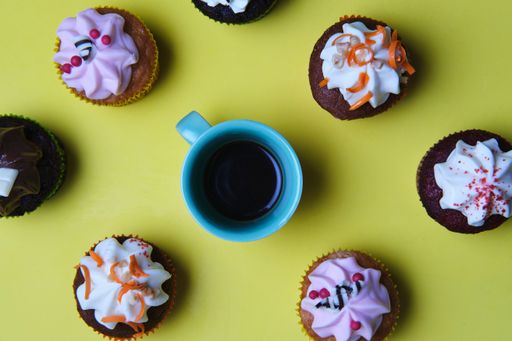 A high angle closeup shot of small cupcakes with colorful creams and a cup of coffee on a green surface