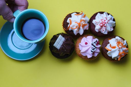 A high angle closeup shot of small cupcakes with colorful creams and a cup of coffee on a green surface