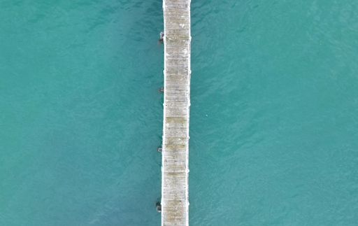 An aerial top shot of a pier over the teal water