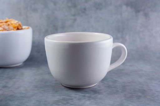 A closeup shot of a small white mug isolated and a bowl of cereal on a gray background