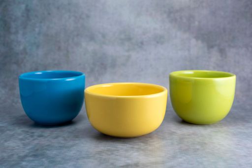 A set of ceramic yellow, green, and blue bowls on a gray background