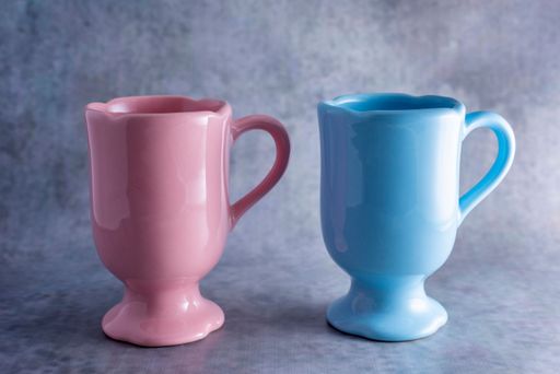 A closeup shot of a pink mug and a blue mug isolated on a gray background