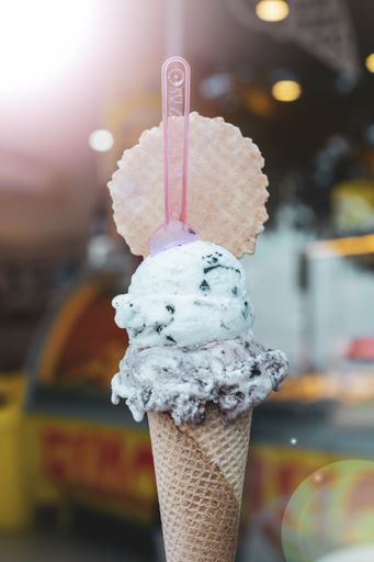A vertical selective focus shot of mint chocolate chip ice cream scoops on a cone with a pink spoon and a waffle