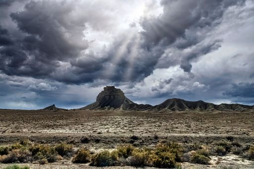 A Shiprock view with gloomy and cloudy sky with sun rays shining through and brightening around, New Mexico