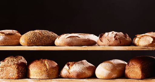 A bunch of appetizing freshly baked loaves of bread on wooden shelves against a black background.
