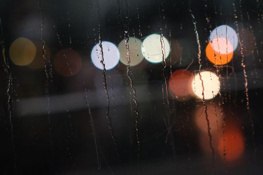A close-up shot of a wet window surface in rainy weather in the background of bokeh lights
