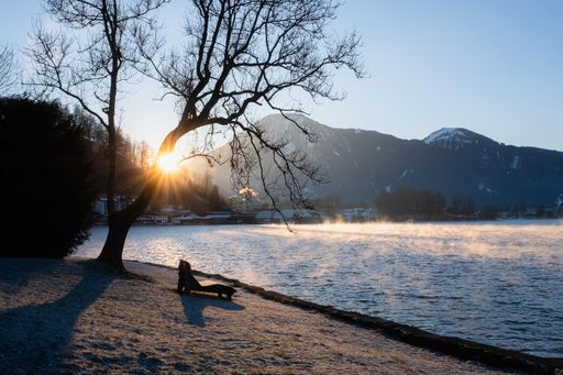A scenic view of a bench at the lakeshore with mountains in the background