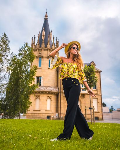 A beautiful shot of a blonde woman in a yellow vintage outfit with a hat posing on a castle background