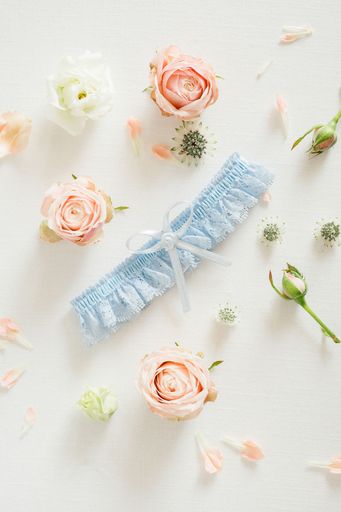 A vertical flat lay of a blue wedding garter and roses