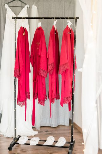 A vertical shot of a hanger with red dressing gowns and a wedding dress in the background
