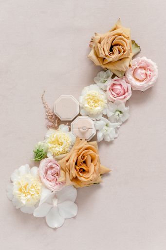 A flat lay of a wedding ring surrounded by flowers on a cream background