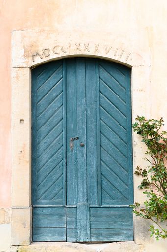 A vertical shot of an ancient house with a blue wooden door and a Latin inscription on it