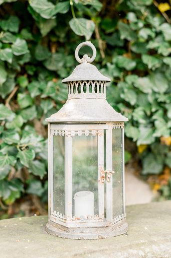 A vertical closeup shot of a white decorative lantern with a candle in it on a sunny day in a garden