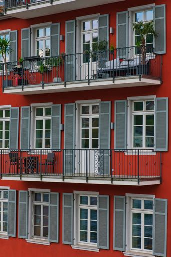 A vertical shot of a red building facade with gray window covers and balconies