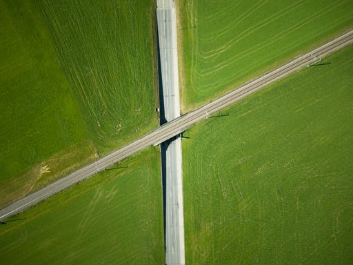 An aerial view of the railroad over the highway surrounded by green fields