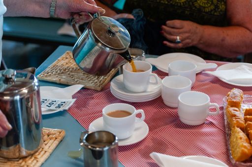 A female hand pouring tea from a teapot into white cups on a table
