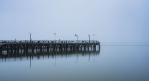 A scenic shot of a dock reflected in the river on a foggy day
