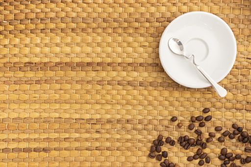 A high angle shot of a nice spoon and a plate, some coffee beans on a woven surface