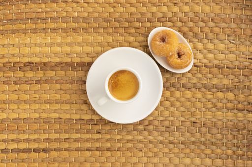 A high angle shot of a cup of coffee and two donuts on a woven surface