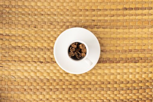 A high angle shot of cinnamon sticks in an empty cup on a woven surface