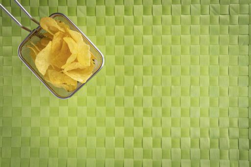 A high angle shot of a basket of potato chips on a woven green surface